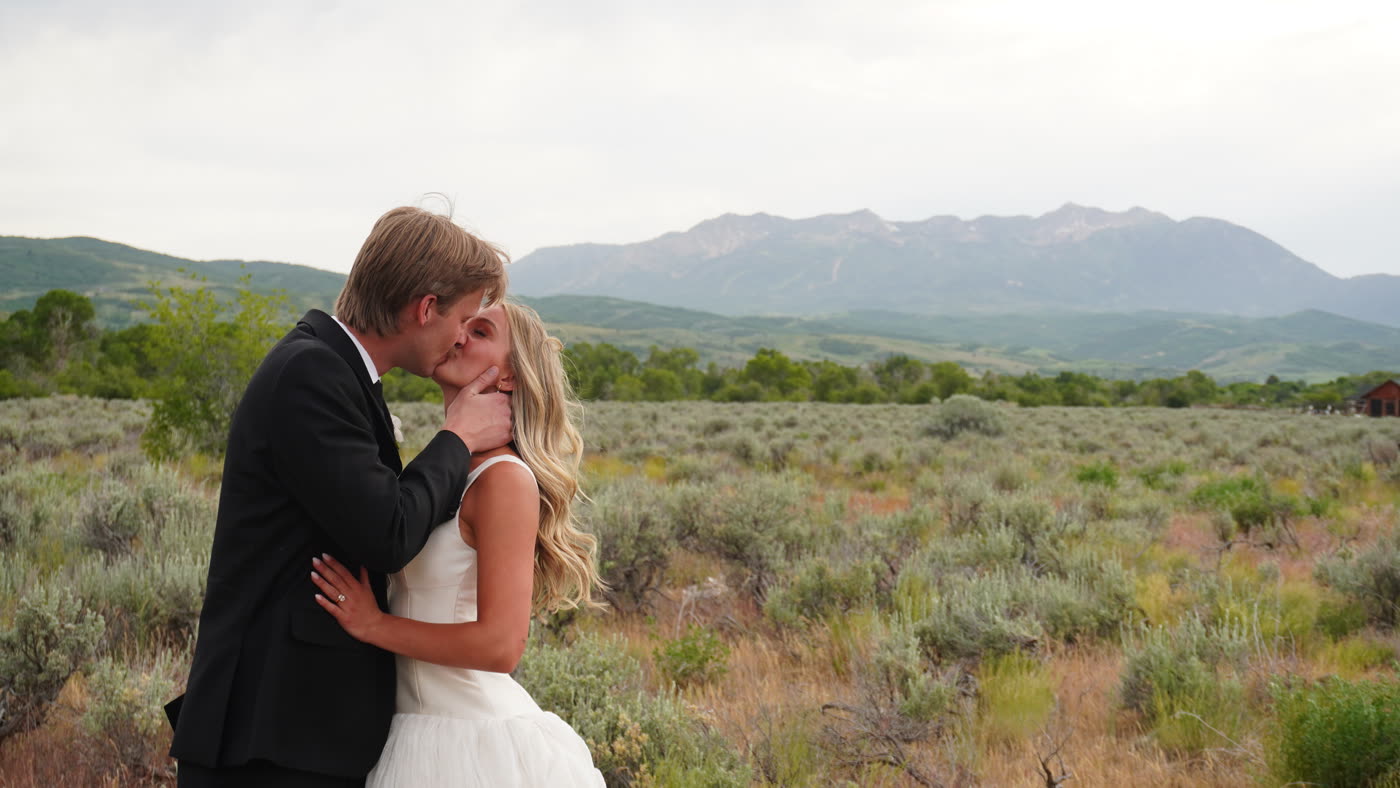 Bride and groom kissing in a mountain meadow, captured by the outdoor Glam booth